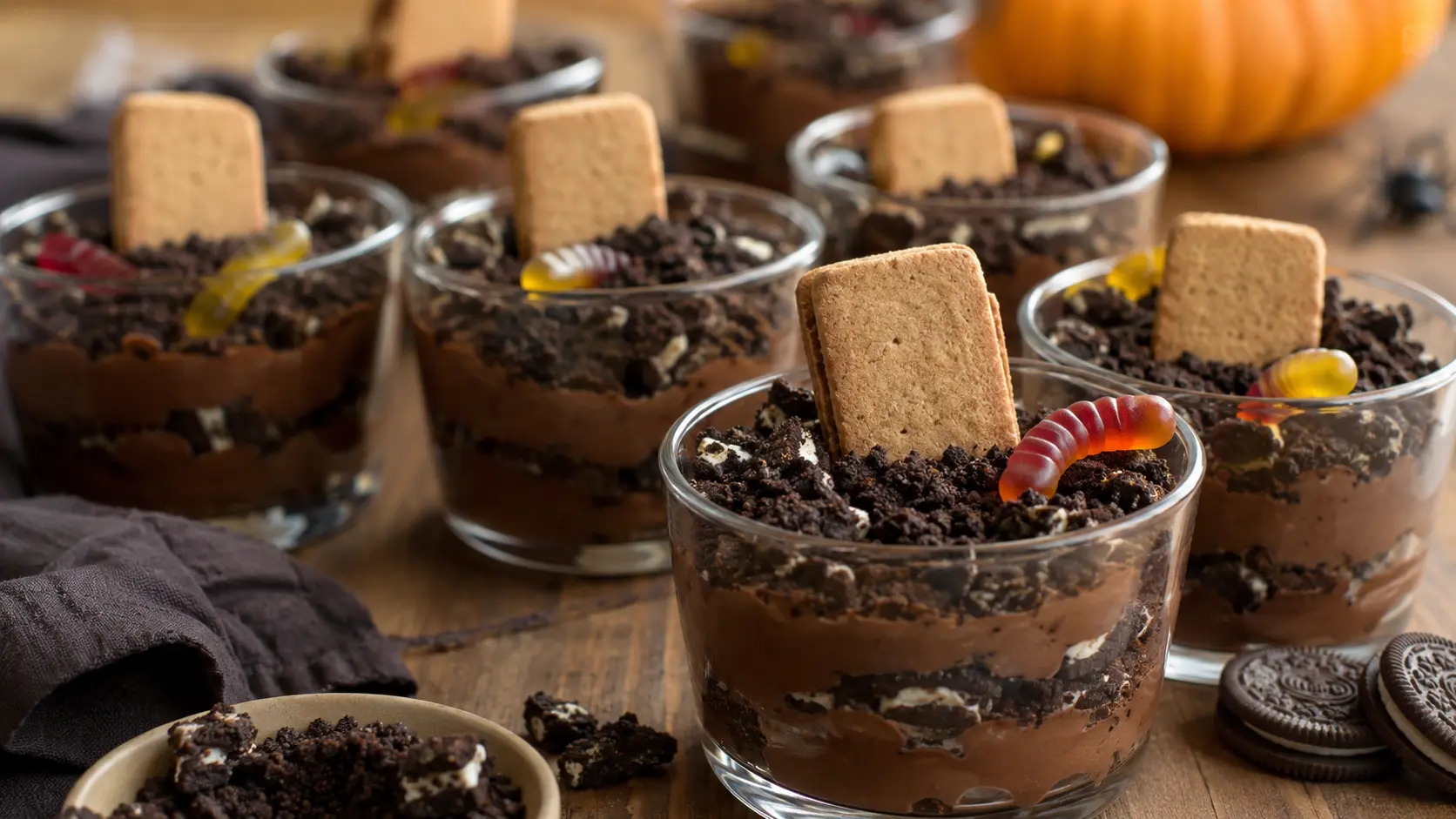 Homemade Halloween graveyard dirt cups with creamy chocolate pudding, crushed chocolate cookie dirt, gummy worms and cookie tombstones.